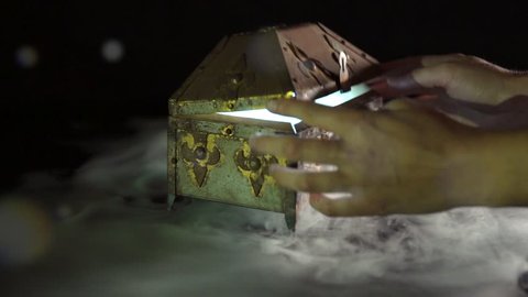 4K anonymous hands opening mysterious treasure chest / pandoras box with glowing mist / fog / smoke inside on black background