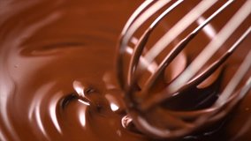 Chocolate. Mixing melted liquid premium dark chocolate with a whisk. Close up of liquid hot chocolate swirl. Confectionery. Confectioner prepares dessert, icing. 4K UHD video, slow motion 120 fps
