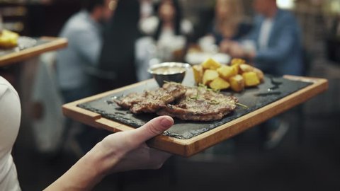 waiter bears a meat dish to the table. the company of friends gathered for dinner in a cafe or restaurant Video de stock
