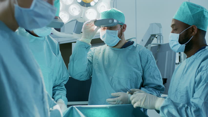 Surgeons Wearing Augmented Reality Glasses Perform State of the Art Mixed Reality Surgery in High Tech Hospital. Doctors and Assistants Working in Operating Room. Shot on RED EPIC-W 8K Helium Camera. - Powered by Shutterstock - Get 15% off with code: PIKWIZARD15