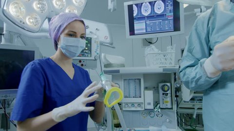 In the Hospital Operating Room Anesthesiologist Applies Anesthesia Mask to a Patient, Assistants Disinfects with Iodine place of Incision, Surgeons Wait to Start Surgery. Shot on RED EPIC-W 8K Camera.