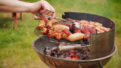 Close up of woman s hand holding a tongs turning the grilling sausages on barbecue grill