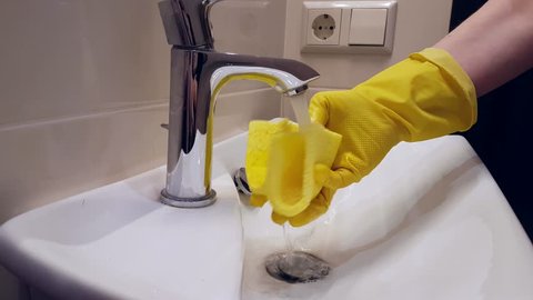Hands in gloves wash the sink in the bathroom