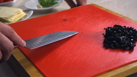 A professional chef cutting capers on a red cooking board very quickly. The preparation of food for cooking vegetarian dishes. The salted and pickled caper bud is often used as a seasoning or garnish.