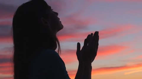 Woman praying looking up with hands open to sky silhouette beautiful sunset