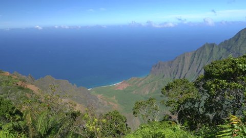 Magnificent view of amazing canyon valley with lush rainforest jungle overlooking crystal clear ocean bay. Beautiful nature at mountain top lookout point along the famous Kalalau trail in Hawaii