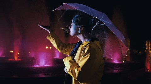 Young pretty girl with blue dyed hair checks to see if it's raining near fountain. Night illumination of city. Portrait of stylish hipster with glasses. Video de stock