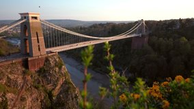 Camera slides over hedgerow with the Clifton Suspension Bridge behind. Shot during a spring sunset with a hot air ballon in the sky