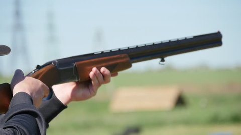 Closeup of a hunter keeping his modern double barrel gun, targeting and shooting at clay plates. The recoil rocks the rifle on a range in slo-mo