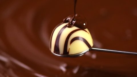 White chocolate truffle candy covered dark chocolate on brown background with swirls. Melted Chocolate pouring on praline candy close up. Dessert. Gourmet food. 4K UHD video