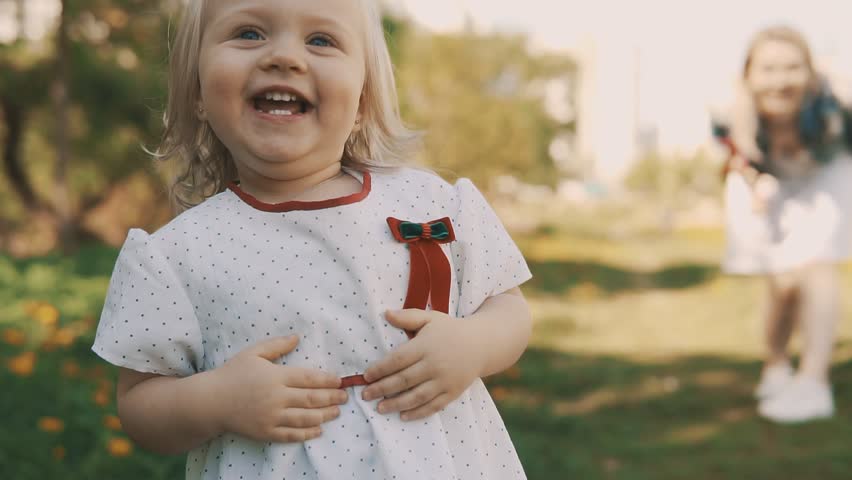 Funny Little Girl Running Away from Her Mom. Mother and Daughter in Dress Playing Together Enjoying Warm Summer Weather in Park in Slow Motion