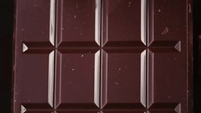 Melted dark chocolate pouring on whole chocolate bar. Confectionery concept backdrop. Sweet dessert background. 4K UHD video, slow motion