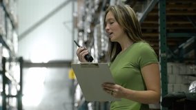 Woman talking into a hand held radio system and holding a clip board in warehouse.
