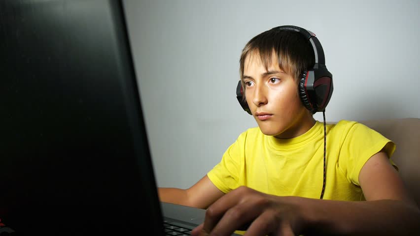 Teenager using laptop at night time. Computer addicted teen boy with a poker face looking at the notebook screen pressing the keyboard | Shutterstock HD Video #1011085553