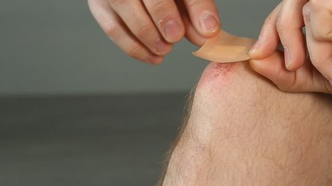 Man opens and applies an adhesive sticking bandage to an injured knee with a wound. Leg with the abrasion or scratch, scrape. The bactericidal emplastrum medical plaster