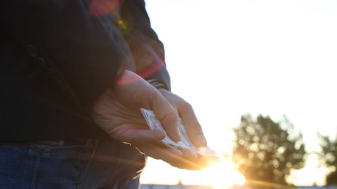 A man in a jacket holds money dollars in handcuffs, close-up, sunset, arrest, handcuffs