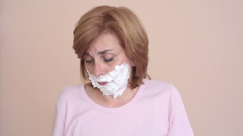 Unhappy middle aged woman with shaving foam on her face holding a razor