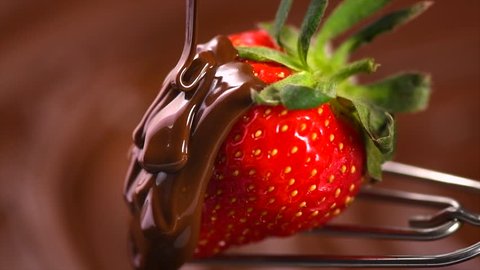 Strawberry in chocolate over swirl brown background. Melted Chocolate pouring on fresh ripe juicy strawberry close up. Dessert. Gourmet food. Fondue. 4K UHD slow motion video