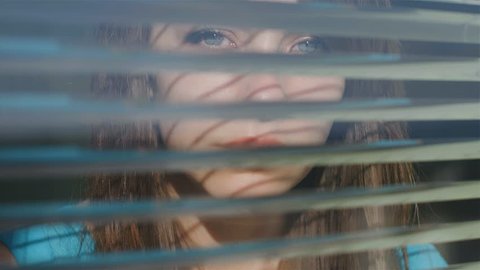 COVID 19 Isolation Concept. Stay at home quarantine. Beautiful young woman looking out the window through the blinds to the street.