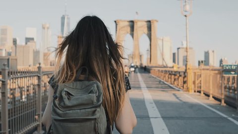 Camera follows young woman with backpack walking along Brooklyn Bridge, New York on a beautiful sunny summer day 4K.