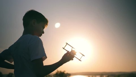 A child is playing with a toy airplane at sunset. Silhouette of a boy holding a toy, hand holding a small airplane. The dream of flying and traveling Stockvideó