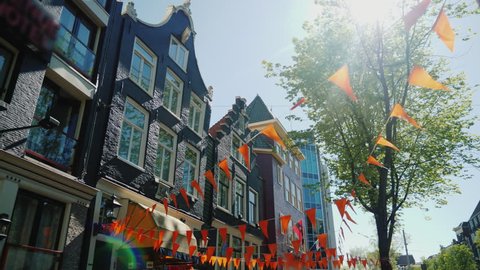 Amesterdam, Netherlands, May 2018: Walking in the streets of Amsterdam. Old houses and triangular orange flags at the top. Steadicam pov video, low angle shot