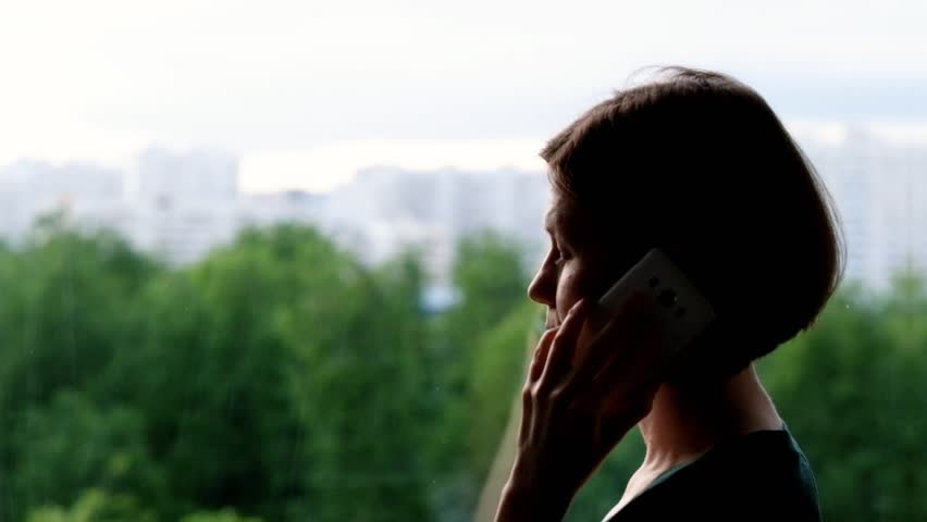Woman standing at the window and talking on the phone, depressed | Shutterstock HD Video #1011133223