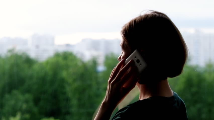 Woman standing at the window and talking on the phone | Shutterstock HD Video #1011133244