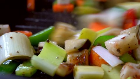 Vegetarian vegetables are fried on a grill pan. Professional chef mixing colored vegetables with a spatula. Macro oil splashes on the pan. Carrot, leek, eggplant, zucchini, sweet pepper, chili pepper.