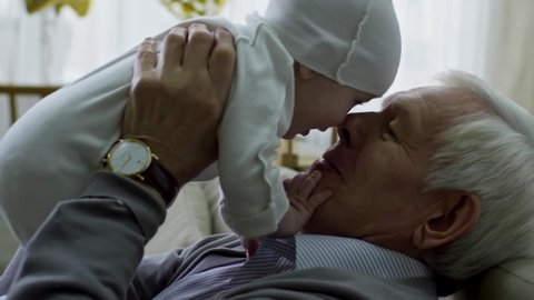 Tilt up of happy grandfather with grey hair playing with adorable baby boy while babysitting