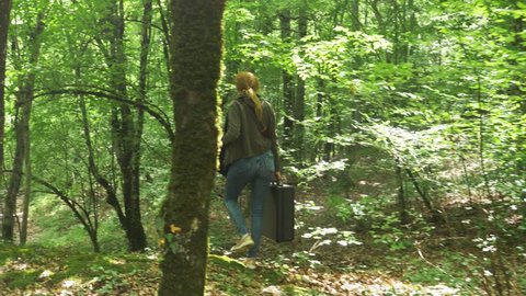girl, walks through the woods with a heavy black suitcase. 4k, slow-motion shooting, steadicam shot.