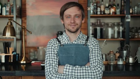 Portrait of smiling owner standing at his restaurant gate. Young entrepreneur leaning at the cafeteria door and looking at camera. Chef or waiter standing in front of coffee shop.