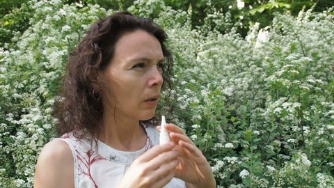 Allergy to pollen. A woman with allergies in nature. A sick woman splashes nose with medicine.