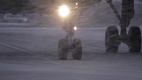 Slow motion shot of airplane wheels moving on runaway. View in evening blizzard