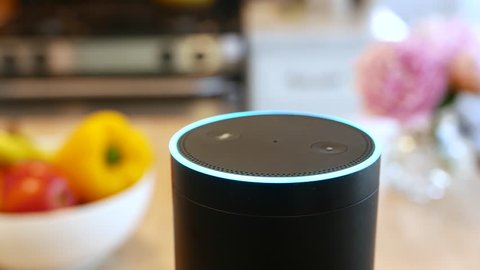 Amazon Alexa closeup in a kitchen.  Pretty flowers and fruit in Background.  Smart speaker activates in a kitchen environment. For editorial use.