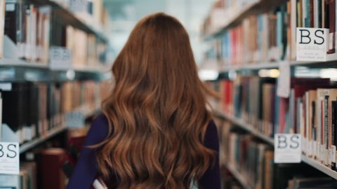 UKRAINE, LVIV - MARCH 26, 2018: Girl with long hair walks along the shelves in the library. Concept: educational, library, studious and portrait
