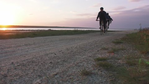 Two young men riding bicycles on the beach on the background of an orange sunsetting sky