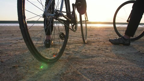 Two young men sitting on bicycles on the beach on the background of an orange sunsetting sky, close up shot
