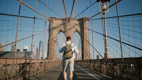 Happy male tourist walking away from camera back view, looking around along Brooklyn Bridge, New York on a sunny day 4K.