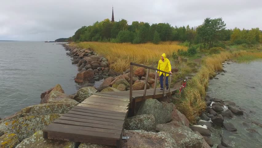 A sailor in a yellow raincoat rises to a stone dock