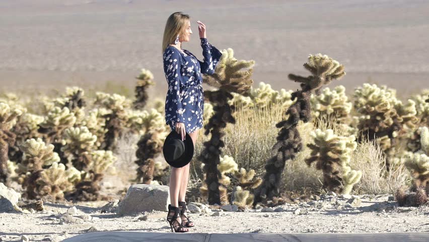young woman with a hat in the hands at the side of the road in the desert