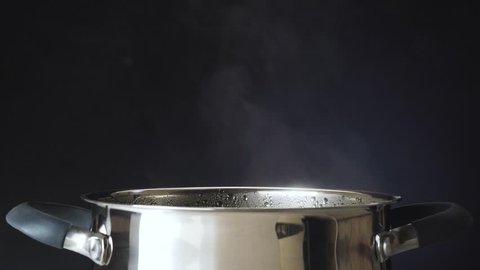 The cook salt the soup. The pan is on the stove. Steam comes from the pan. 4k