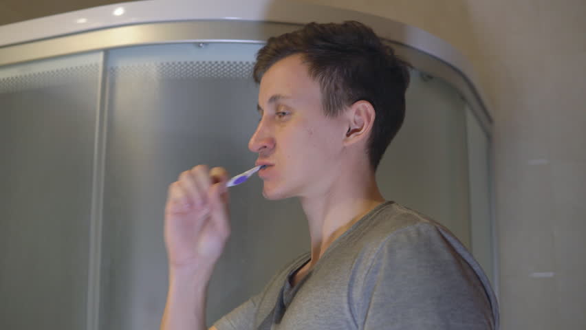 Man is brushing his teeth in the bathroom.