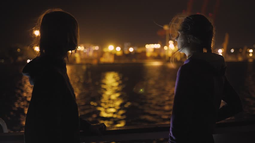 Silhouette of two attractive young women traveling on a ship at night. 