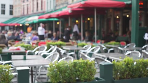 Out of focus background plate of row of European cafe patios for compositing. Defocused video backdrop of tables and chairs outside coffee shop for green screen. 4k