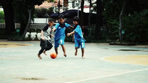 JAKARTA, INDONESIA - FEBRUARY 11, 2018: A group of Indonesian children play football in slow motion at Menteng Park, Jakarta.