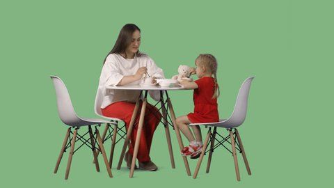 Mather with the little daughter are sitting at the table and drink a tea. Green screen footage. File format - .mov, codec PNG+Alpha. 85 mm lens