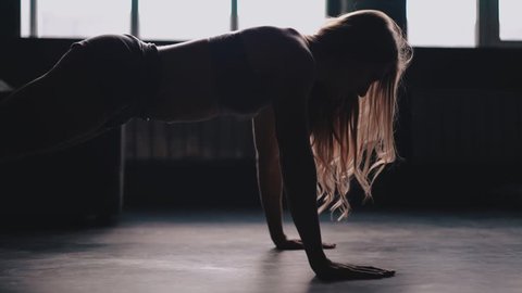 Unrecognizable attractive young woman wearing a gray sports bra and shorts doing pushups in a gym. Slow motion handheld medium shot