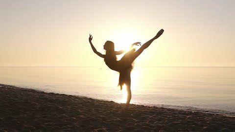 Silhouette of an elegant ballerina in a tutu in the rays of the morning sun. Doing exercises, practicing. Seashore. Slow motion