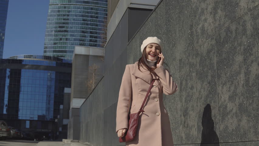 Woman in a coat goes to the center of the city, talking on the phone.
